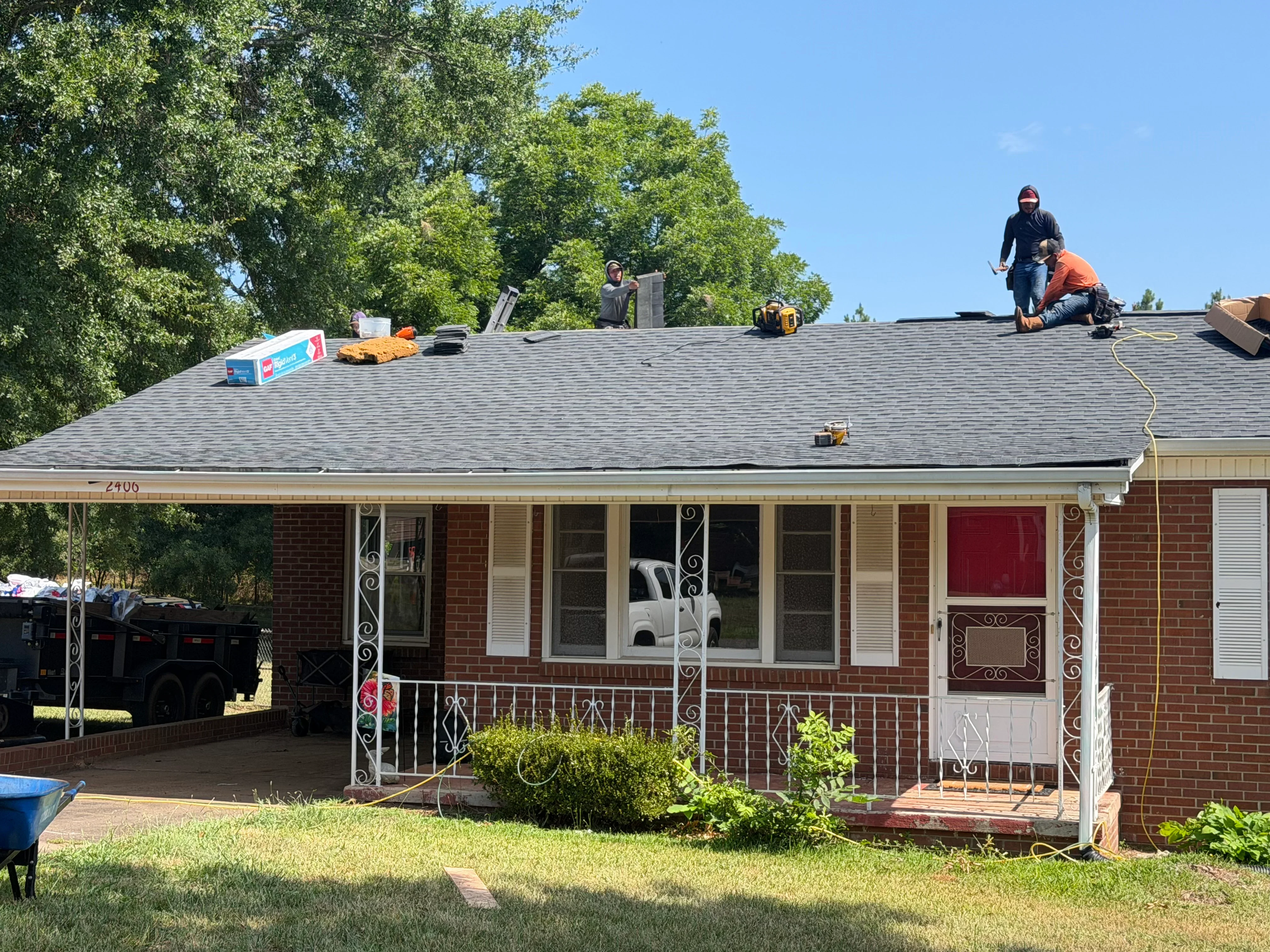Roofers installing new gray architectural shingles on brick home in Shelby