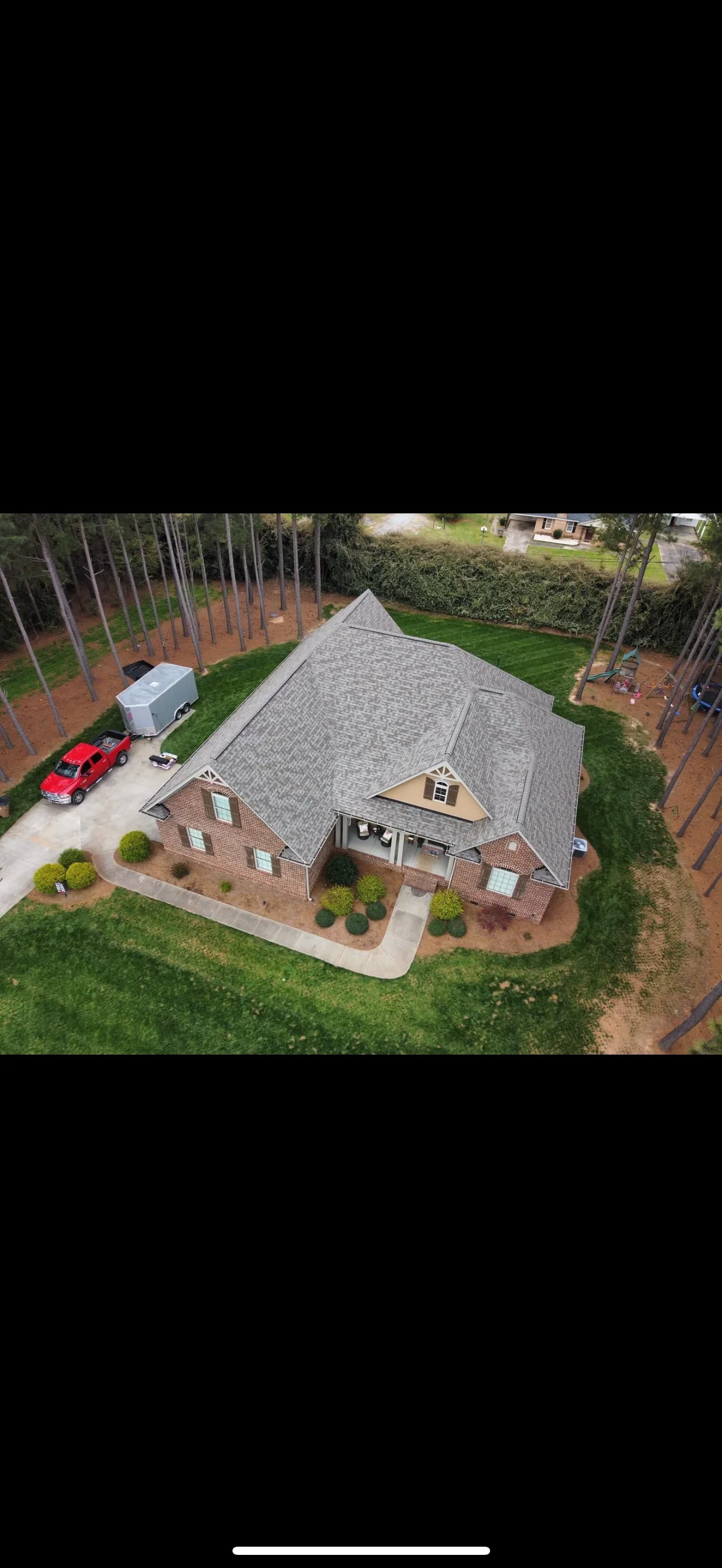 Aerial view of brick home with new gray architectural shingle roof and manicured landscaping