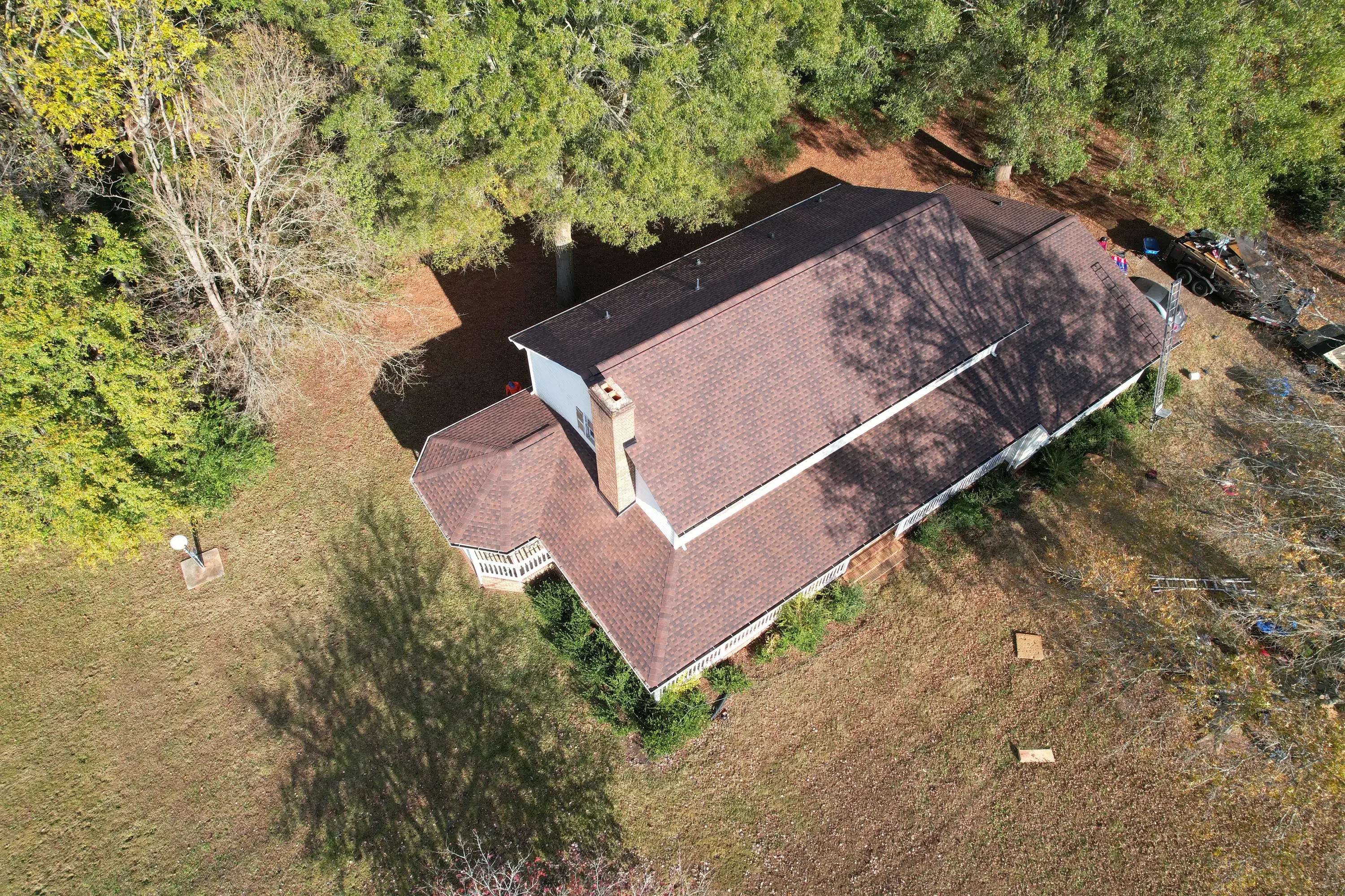 Aerial view of residential home with new brown architectural shingle roof in wooded setting