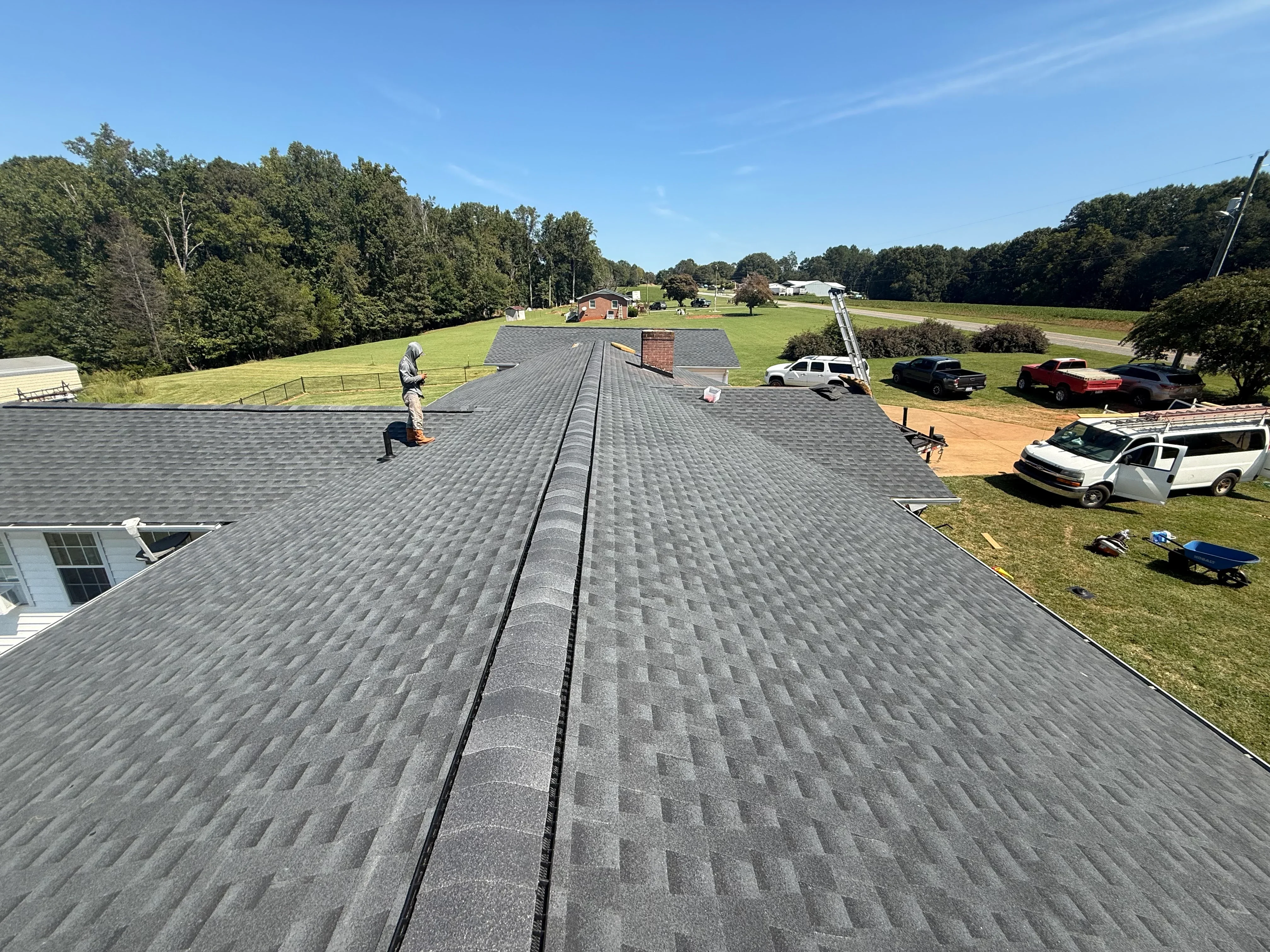 Roofer installing gray asphalt shingles on large residential roof with ridge vent