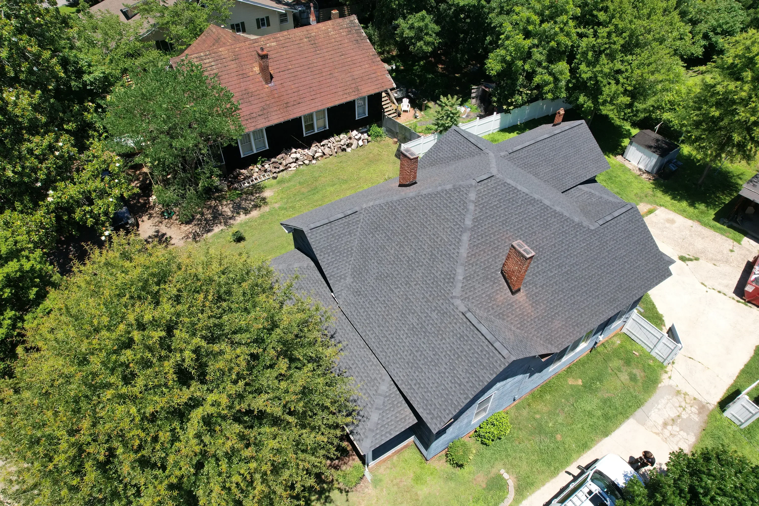 Aerial view of completed residential roof with gray shingles and brick chimneys
