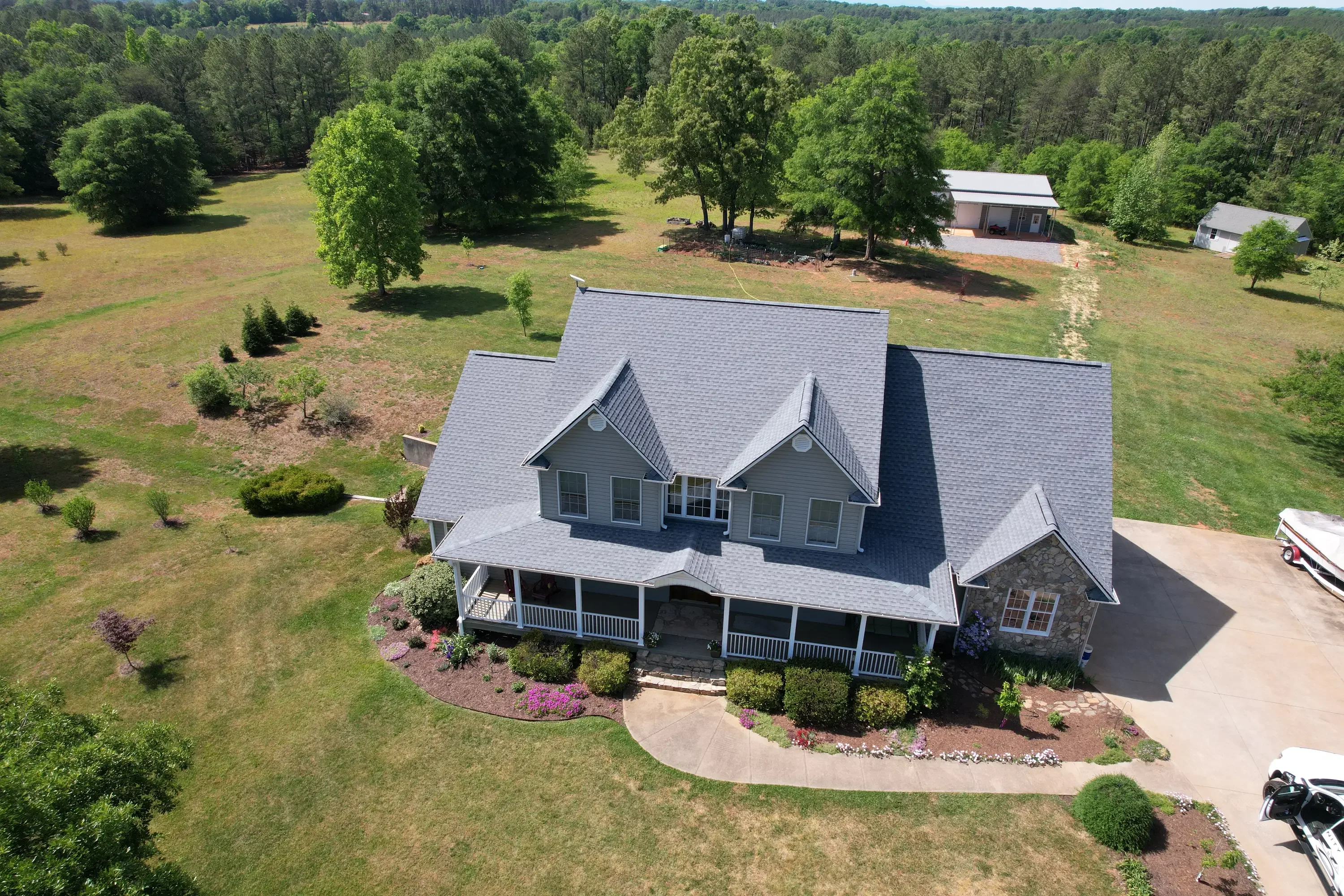 Aerial view of gray architectural shingle roof on two-story home with wrap porch and stone chimney