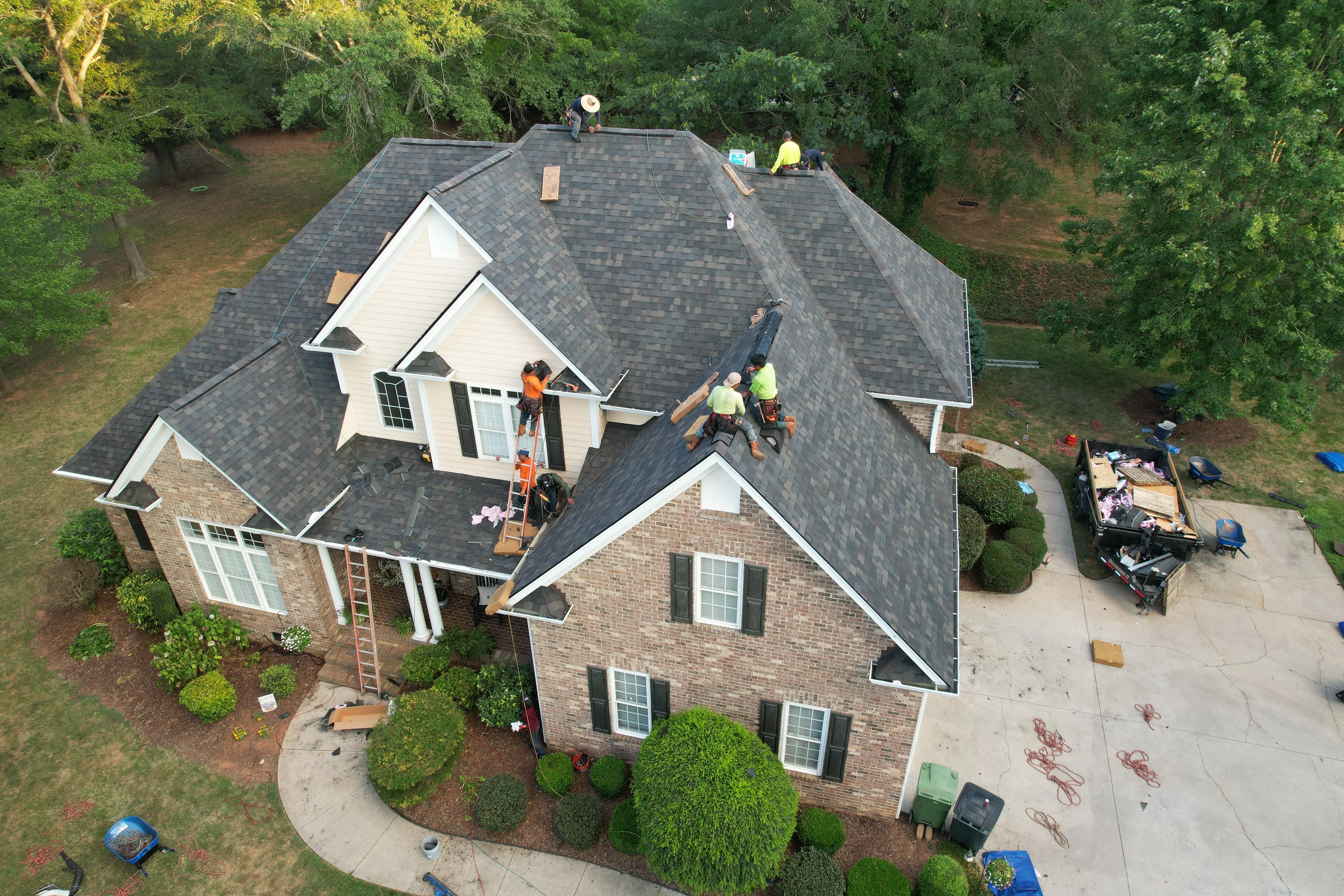 Aerial view of brick home with new gray architectural shingle roof installation in progress
