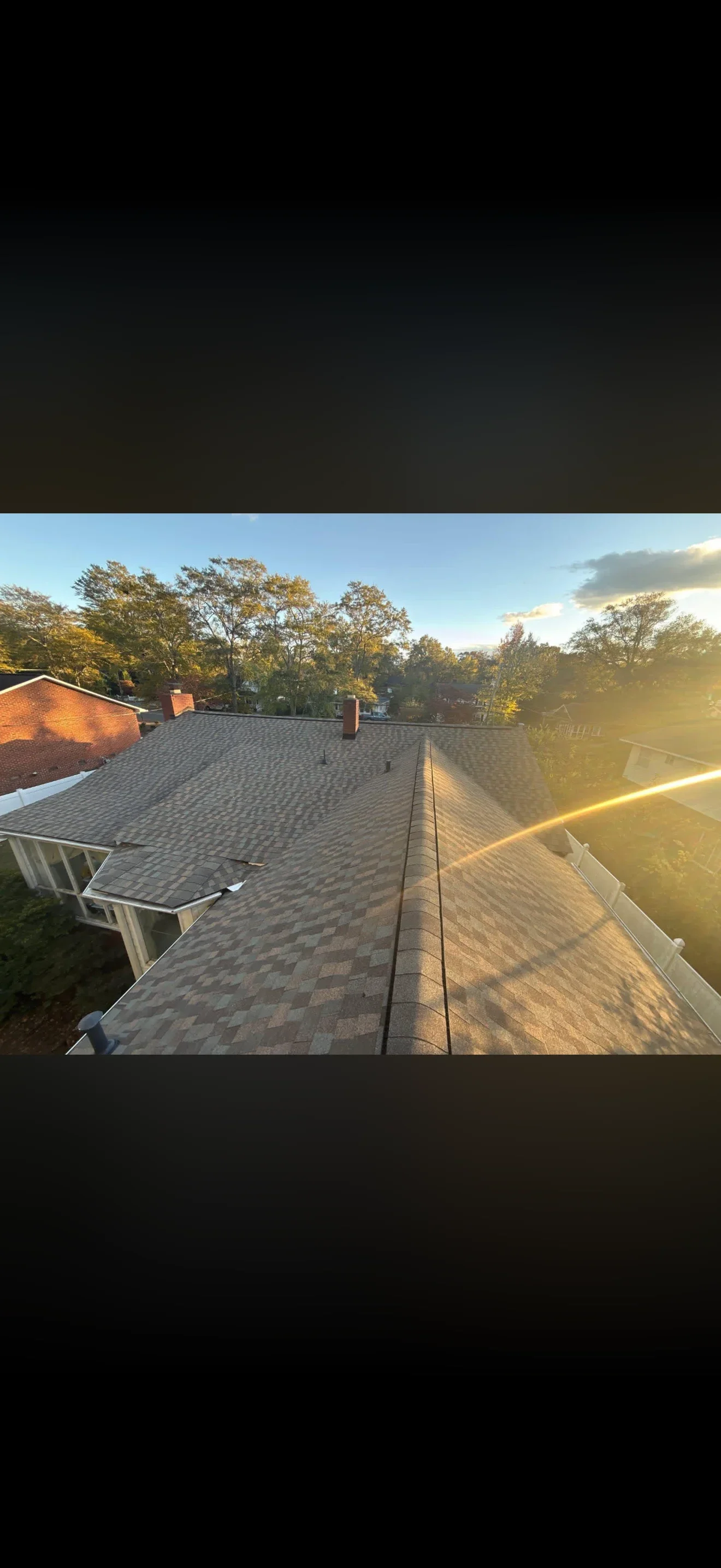 Newly installed gray architectural shingle roof with brick chimney and white gutters at sunset