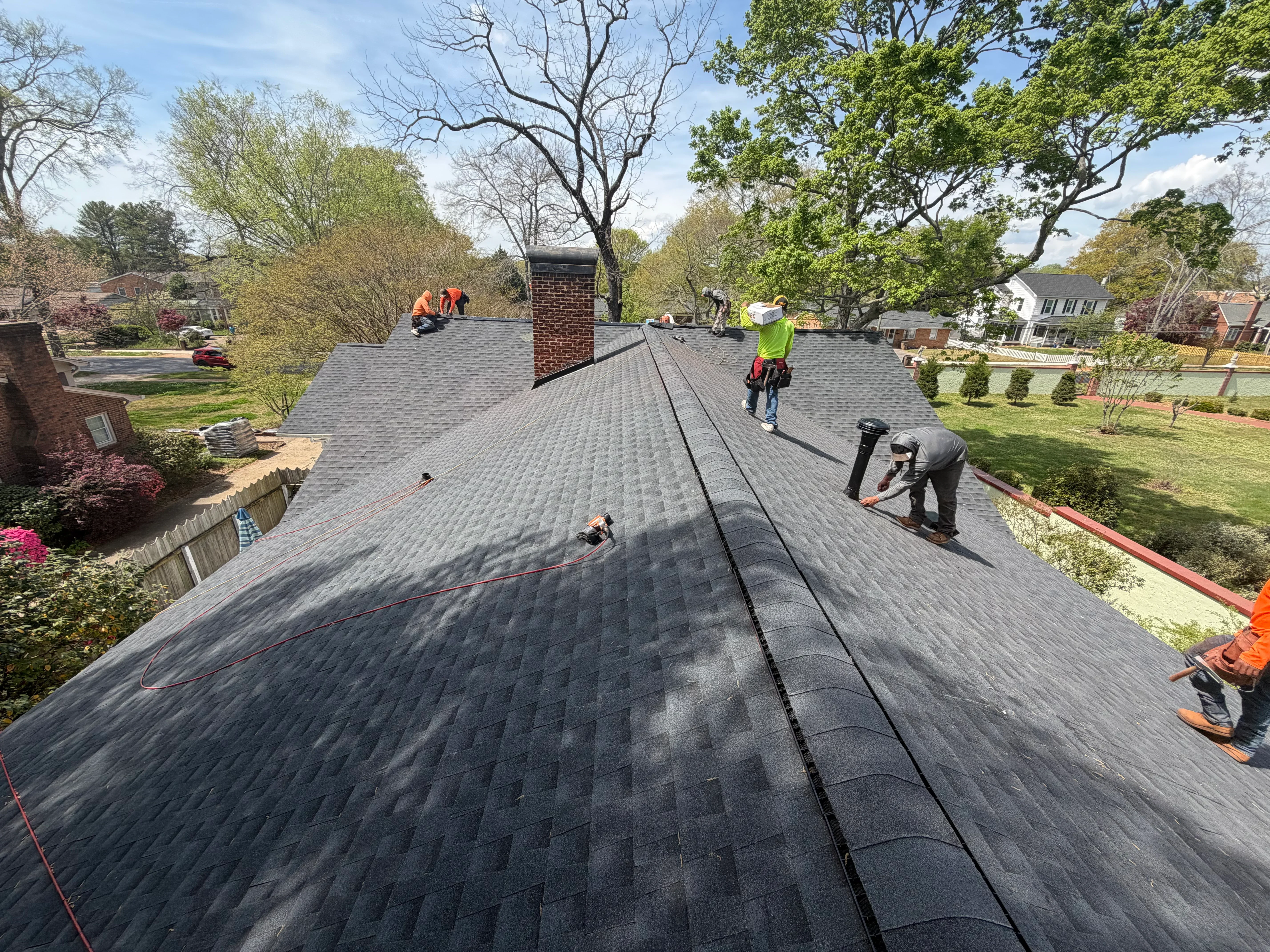 Roofers installing gray asphalt shingles on residential home with brick chimney in Shelby